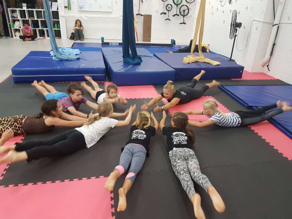 A group of workshop participants stretch and warm up before participating in circus activities. An essential part of any school holiday workshop or activity