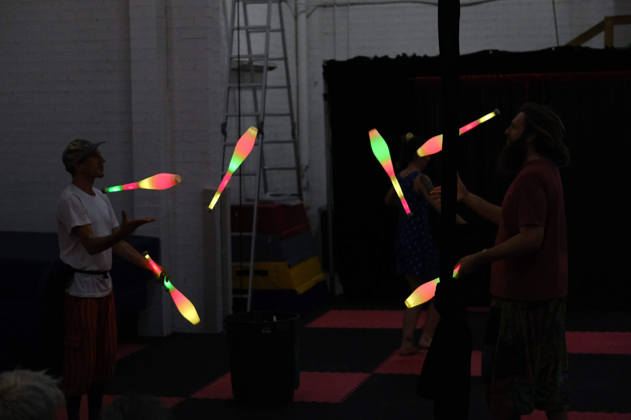 two circus performers partner juggle with glow clubs