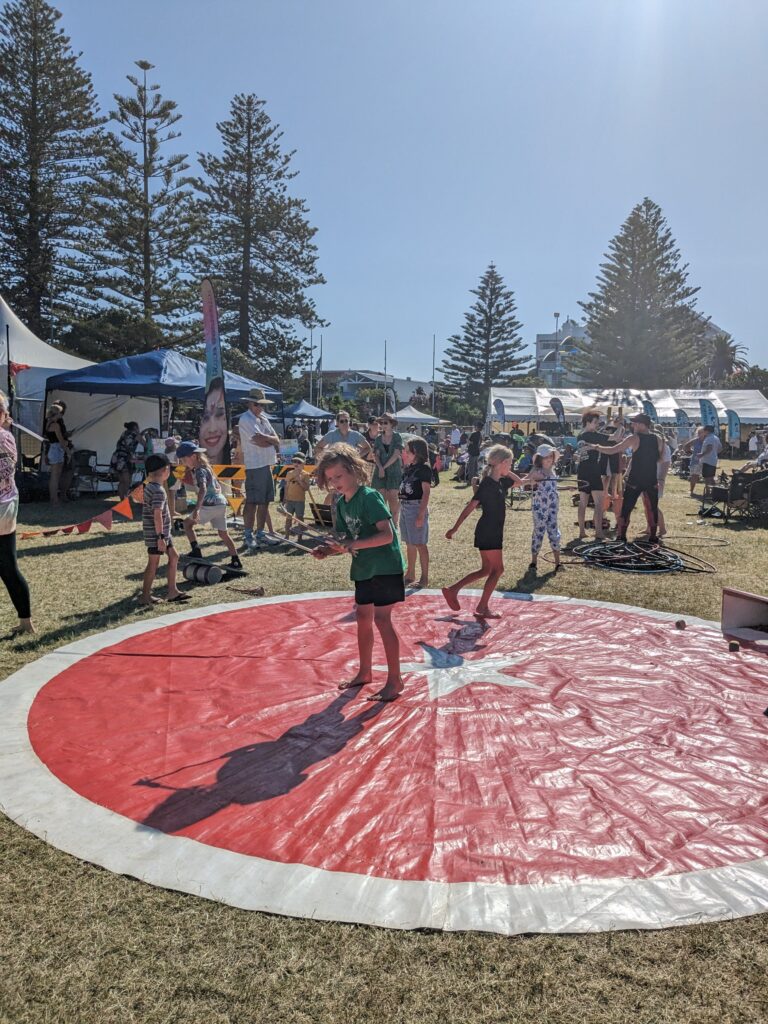 A child stands on a large red circle mat with a white star on it, playing in the Roundabout Circus play space at Girrakool Blues festival.
