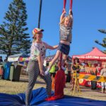 Child performer with trainer assistance at Girrakool Blues festival, doing a circus trick in aerial silks