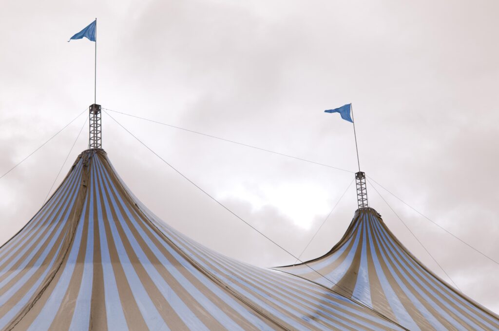 Colourful striped red and white big top tent at a circus flying two flags from the centrs poles against a cloudy sky. Bif top tent at a circus. Canvas, entertainment, marquee, performing, striped, tent, acts