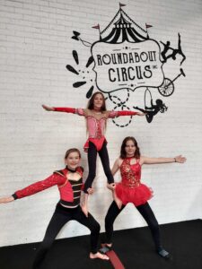 Three Roundabout Circus students perform a three person pyramid in front of the Roundabout Circus sign at the studio in Wyoming.