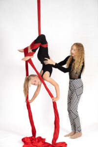 A student receives assistance from a talented trainer in how to hold their body for an inverted silks trick. Roundabout Circus in Wyoming New South Wales offers classes on aerial apparatus like silks, lyra and static trapeze.