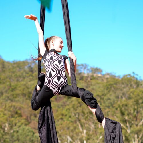 An awe-inspiring shot of a young artist mid-air during a silks act, displaying grace and strength.