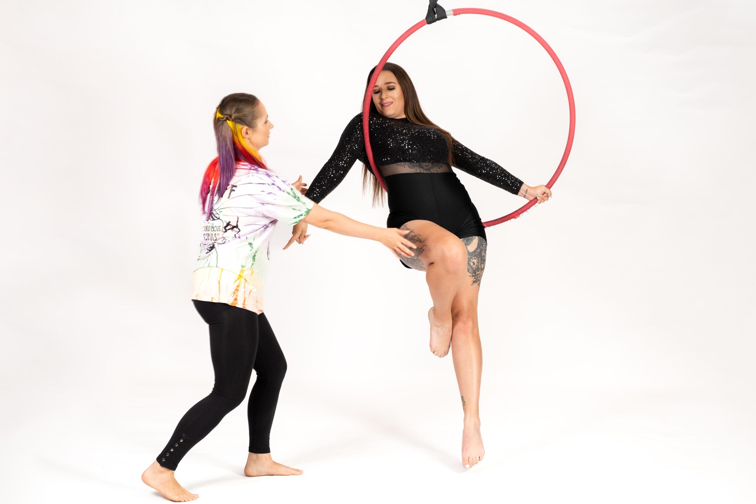 Adult intro to Aerial Lyra An adult sits in a lyra being helped into a photographable pose by a fun creative and inclusive trainer join the roundlings and elevate your fitness game