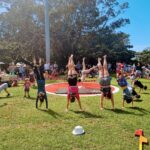 Several people doing handstands in a circle together in a grassy field around a circus tarp.
